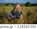 A smiling woman farmer checking the quality of rapeseed, standing at the rapeseed field and holding a laptop 118281302