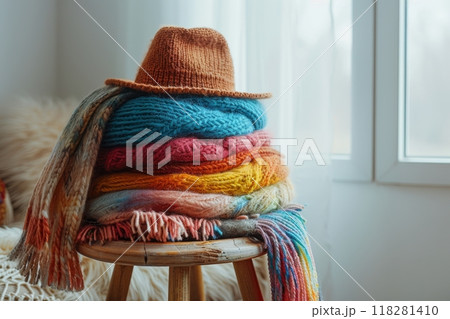 Warm, colored, knitted things, scarves, sweaters folded stack on wooden stool in the living room, bright autumn clothes and accessories Warm, colored, knitted things, scarves, sweaters folded stack on wooden stool in the living room, bright autumn clothes and accessories 118281410
