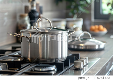 Close up of one grey large stainless steel pots with closed lids on kitchen stove, table well lit daylight from window. New clean kitchen utensils for canteen 118281488