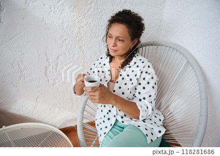 Woman sitting in a modern chair enjoying a cup of coffee in a relaxed setting with a thoughtful expression 118281686