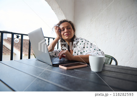 Woman relaxing on outdoor patio with laptop, enjoying peaceful work-from-home setup Woman relaxing on outdoor patio with laptop, enjoying peaceful work-from-home setup 118282593