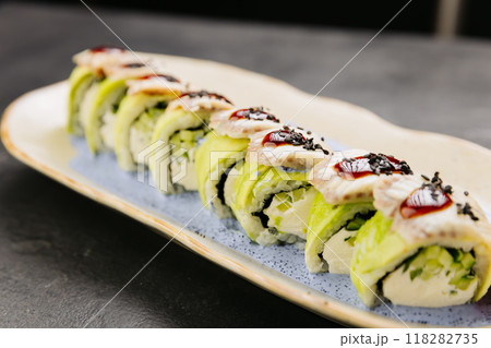 Eel sushi roll with creamy filling, topped with savory sauce and sesame seeds on a stylish plate 118282735