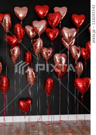 Set of heart shaped air balloons. Bunch of red and pink colour foil metallic balloons on black wall background. Love. Holiday celebration. Valentine's Day, wedding or bachelorette party decoration 118283142