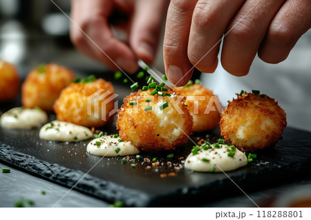Delicate hands artfully garnish golden-hued croquettes on a sleek black serving board in a gourmet kitchen setting 118288801