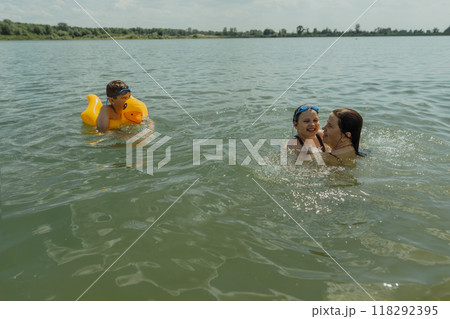 Mom and kids enjoying a summer day at the lakes, swimming and diving in the water. A cheerful and carefree summer day by the lake 118292395
