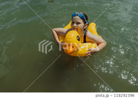 Girl floating in the lake with inflatable yellow duck on a sunny day. Young girl playing with inflatable yellow duck in the water on a sunny day Girl floating in the lake with inflatable yellow duck on a sunny day. Young girl playing with inflatable yellow duck in the water on a sunny day 118292396