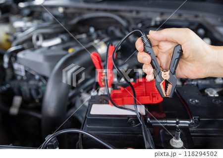 Senior Woman is jumping charger cable to AGM battery on car. 118294502