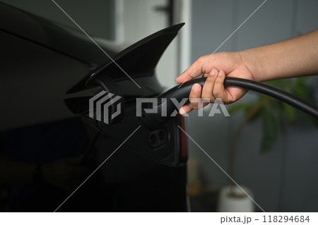Close up of a man plugging charging cable into an electric vehicle a home. Eco friendly transportation concept 118294684