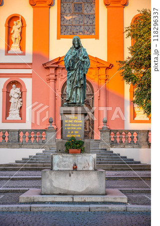 A striking bronze statue of Jesus Christ stands prominently outside the Church of the Assumption of the Virgin Mary in Stara Boleslav, Central Bohemia, surrounded by historical architecture. 118296337