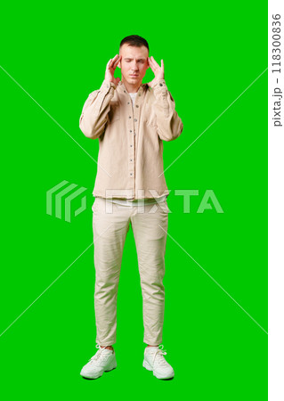 Man With Short Hair Wearing Beige Jacket Holding His Head in Frustration Against a Bright Green Background Man With Short Hair Wearing Beige Jacket Holding His Head in Frustration Against a Bright Green Background 118300836