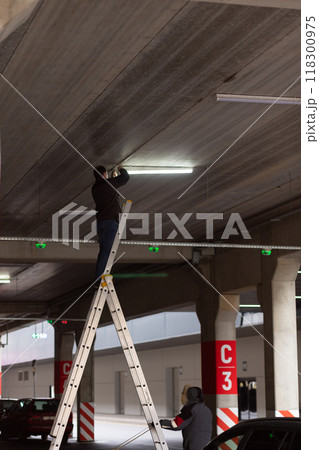 City Worker electrician repairs LCD lamp on mall parking. 118300975