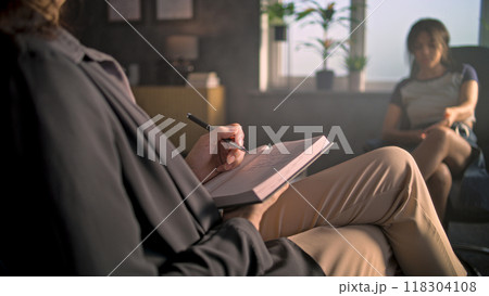 Female therapist takes notes in notebook, listens to upset African American teenage girl Female therapist takes notes in notebook, listens to upset African American teenage girl 118304108