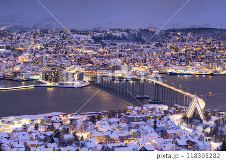 Panorama of Norwegian city of Troms in the winter. Snowy roofs, bridge, embankment near the port and fishing ships. Evening lights Panorama of Norwegian city of Troms in the winter. Snowy roofs, bridge, embankment near the port and fishing ships. Evening lights 118305282