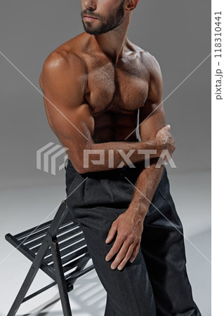 Close-up of man's chiseled chest and abs as he sits with confidence. His focus and posture reflect strength. Close-up of man's chiseled chest and abs as he sits with confidence. His focus and posture reflect strength. 118310441