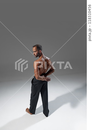 Photo from angle, man looking over shoulder, his back muscles defined in soft light. His body language conveys quiet strength and reflection. 118310456