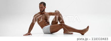Banner. Young man sitting on floor, posing in underwear shows his muscular body against white background with negative space. 118310483