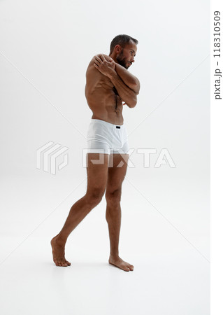 Handsome man stretches his arms over his shoulders, his muscular body against white studio backdrop. Control. Handsome man stretches his arms over his shoulders, his muscular body against white studio backdrop. Control. 118310509