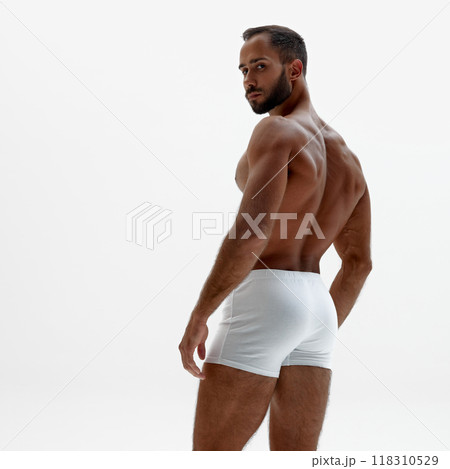 Young man turns slightly, giving view of his broad back and firm posture. His toned muscles against white background. 118310529
