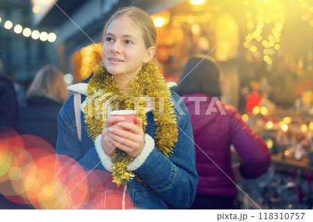 Teenagers girl holding hot cup of coffee in hands at street christmas fair Teenagers girl holding hot cup of coffee in hands at street christmas fair 118310757