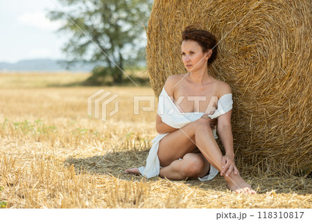Woman with loose hair relaxing near hay bales on summer farm field Woman with loose hair relaxing near hay bales on summer farm field 118310817