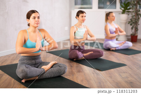 Diligent women practicing lotus pose of yoga in light fitness room 118311203