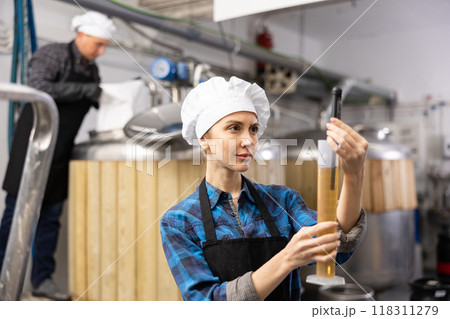 Female brewer using digital hydrometer for measuring beer density 118311279