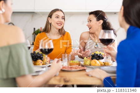 Happy women congregated around a festive table; participating in animated discussions and enjoying the delights of wine Happy women congregated around a festive table; participating in animated discussions and enjoying the delights of wine 118311340