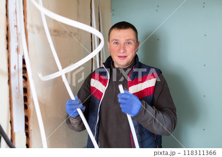 Repair man with cable duct standing in room and looking at camera Repair man with cable duct standing in room and looking at camera 118311366