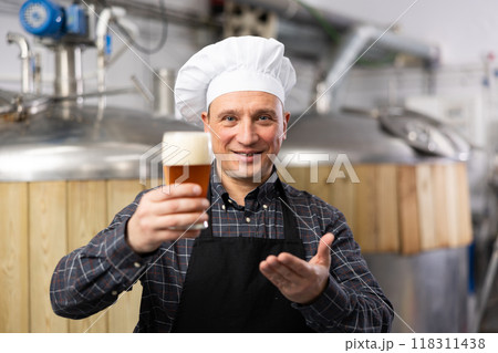 Satisfied professional brewer holding out glass with craft beer 118311438