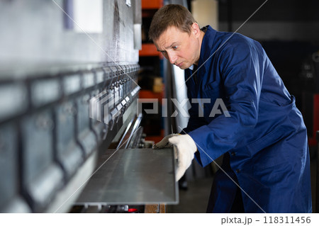 Adult man bends metal sheet under pressure 118311456