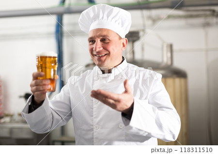 Satisfied professional brewer holding out glass with craft beer Satisfied professional brewer holding out glass with craft beer 118311510