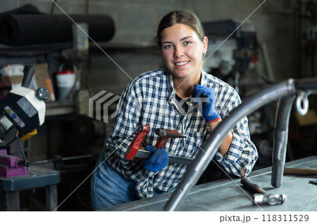 Female technician with clamp in hands posing in metal workshop 118311529