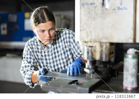 Young female worker operating punch press in metalworking workshop Young female worker operating punch press in metalworking workshop 118311667