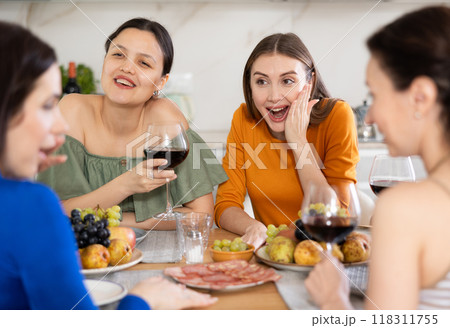 Cheerful female friends enjoying home gathering with wine Cheerful female friends enjoying home gathering with wine 118311755