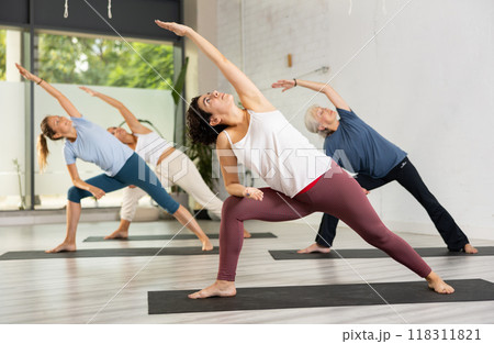 Young Latin female practicing Revolved Side Angle Pose Parivrtta Parsvakonasana, balancing posture of Hatha yoga during group workout in studio 118311821