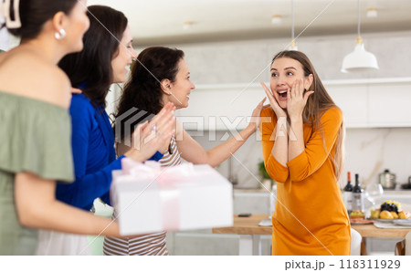 Joyful young woman greeting friends bearing present at home celebration Joyful young woman greeting friends bearing present at home celebration 118311929