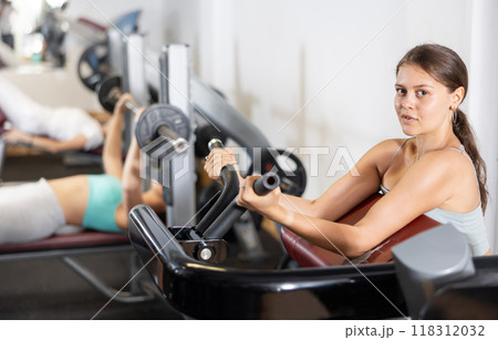 Slender athletic girl work out muscles of arms and shoulders on simulator in gym of fitness club Slender athletic girl work out muscles of arms and shoulders on simulator in gym of fitness club 118312032