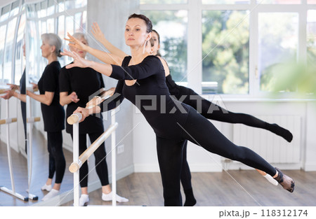 Group of people doing ballet exercises using barre in studio 118312174