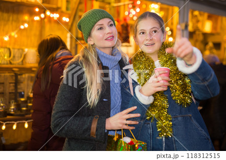 Daughter points her hand to mom as they walk through street Christmas market 118312515