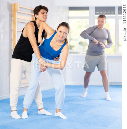 Self-defense class - a woman learns to fight back an attacking man under the guidance of trainer Self-defense class - a woman learns to fight back an attacking man under the guidance of trainer 118312658