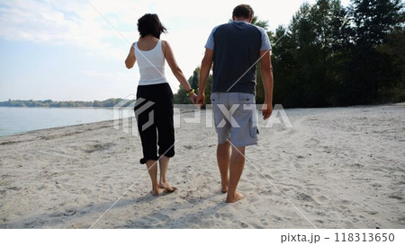 Couple holding hands of each other and walking at coast. Happy pair going along seashore at sunny day. Lovers spending time together at resort. Concept of vacation or holiday. Slow mo Couple holding hands of each other and walking at coast. Happy pair going along seashore at sunny day. Lovers spending time together at resort. Concept of vacation or holiday. Slow mo 118313650