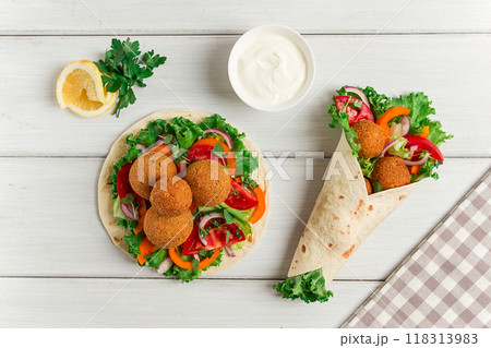 Tortillas, wrapped falafel balls, with fresh vegetables, vegetarian healthy food, on a wooden white background, no people, selective focus. Tortillas, wrapped falafel balls, with fresh vegetables, vegetarian healthy food, on a wooden white background, no people, selective focus. 118313983
