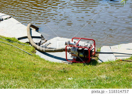 Water pump with a hose on the bank of a pond. 118314757