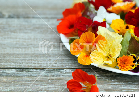 Beautiful healthy vegan salad of lettuce and colorful edible flowers (nasturtium, calendula and pansy) on the wooden garden table. Beautiful healthy vegan salad of lettuce and colorful edible flowers (nasturtium, calendula and pansy) on the wooden garden table. 118317221
