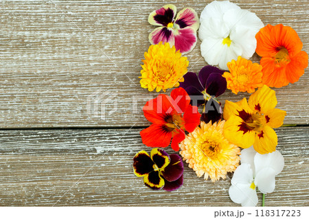 Wooden brown table with edible flowers (nasturtium, calendula, pansy) on the side. 118317223