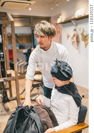 ブランケットを取り、椅子を回転してシャンプー台にお客様を誘導する美容師 118320157