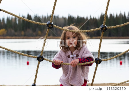 Little girl is on the rope net in the outdoor playground in fall. 118320350