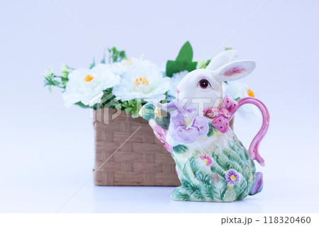 Easter decor with Colorful floral bunny-shaped ceramic saucer near the wicker little basket with white flowers on the background. 118320460