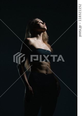 Model striking a pose in dramatic lighting against a dark background Model striking a pose in dramatic lighting against a dark background 118321152