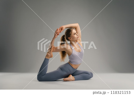 Flexible yoga practitioner elegantly stretches in a serene studio setting 118321153